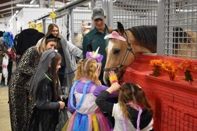 kids in Halloween costumes petting horse in stall